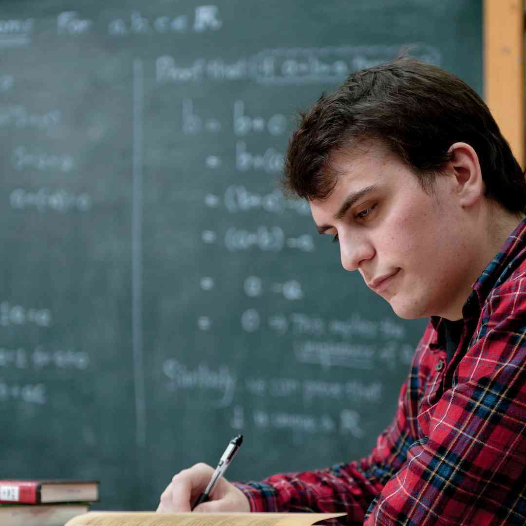 A student writes in a workbook in front of a chalkboard in a classroom
