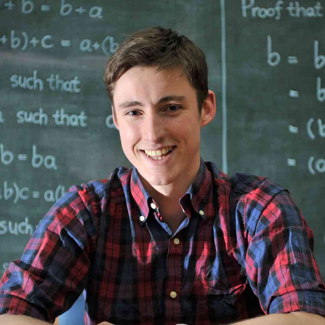 A mathematics student smiling in front of a blackboard with equations