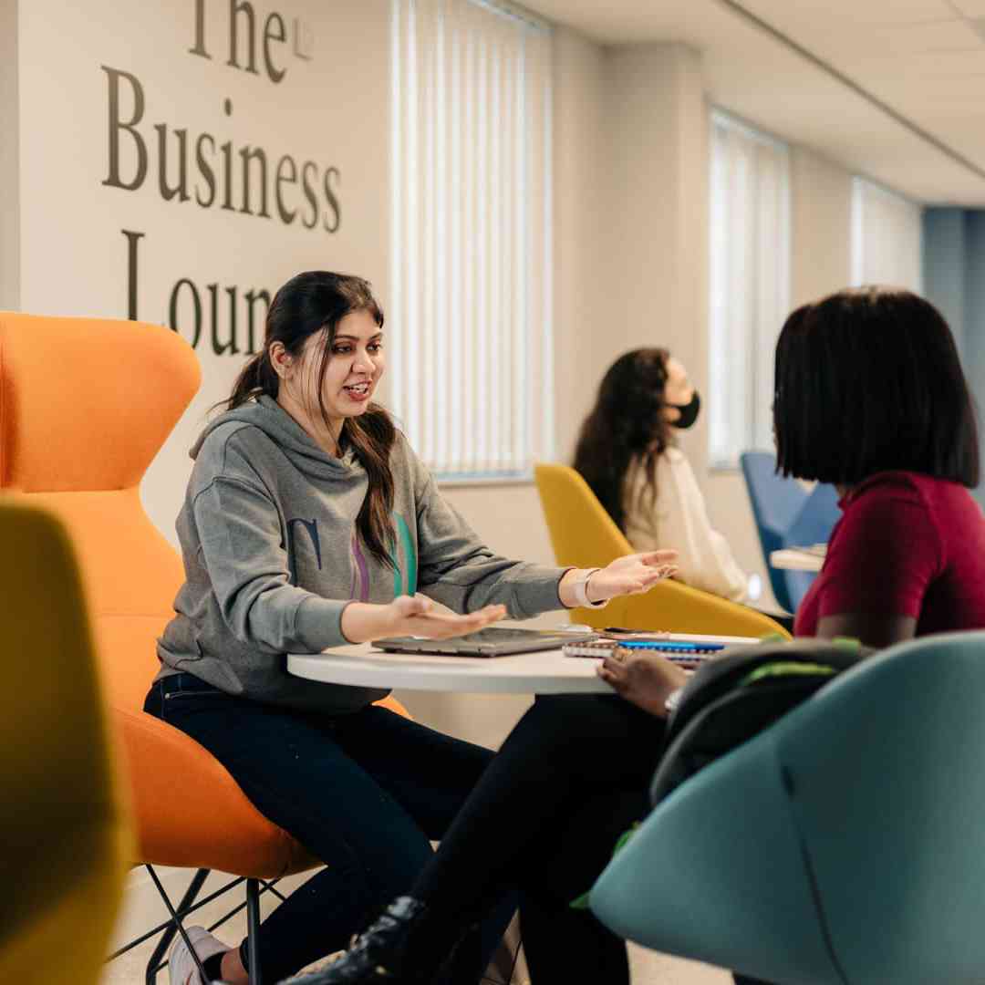 Two female students sat around a table in the Business Lounge