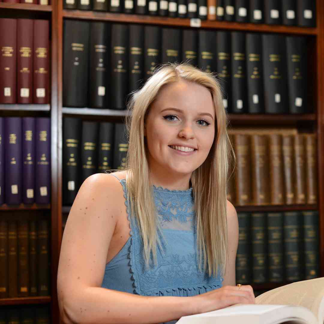 Hull History student, Hannah England, sits smiling with an open book in the Brynmor Jones Library, University of Hull.