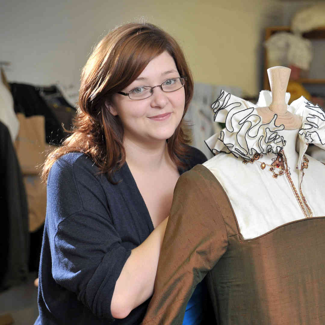 A student is smiling while dressing a mannequin in the costume department of the Gulbenkian Centre, University of Hull. 