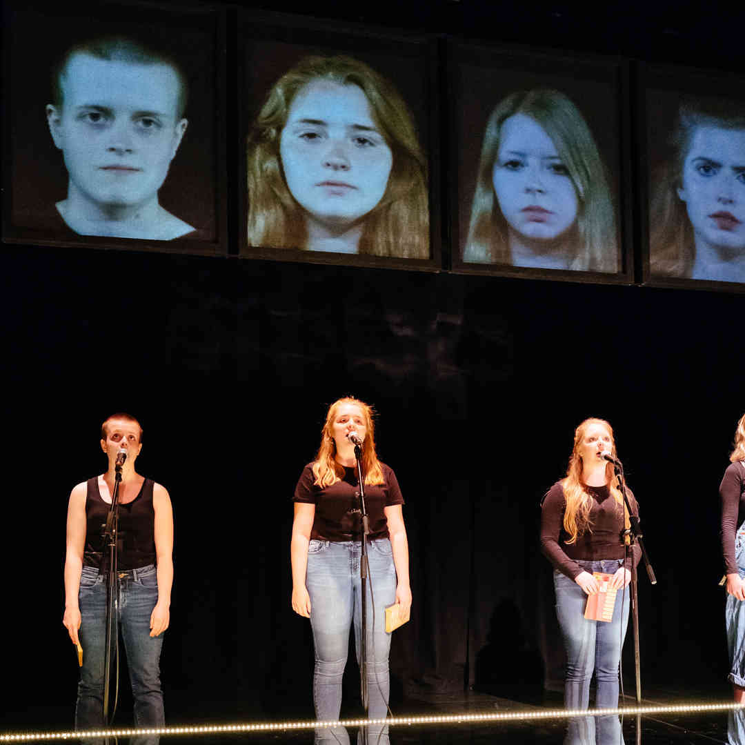 Four students performing with microphones under spotlights on a dark stage. Their portrait photos are above them.