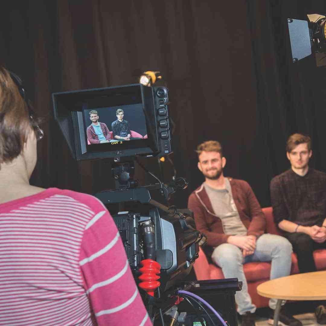 Three students sitting on a sofa are filmed in a TV studio