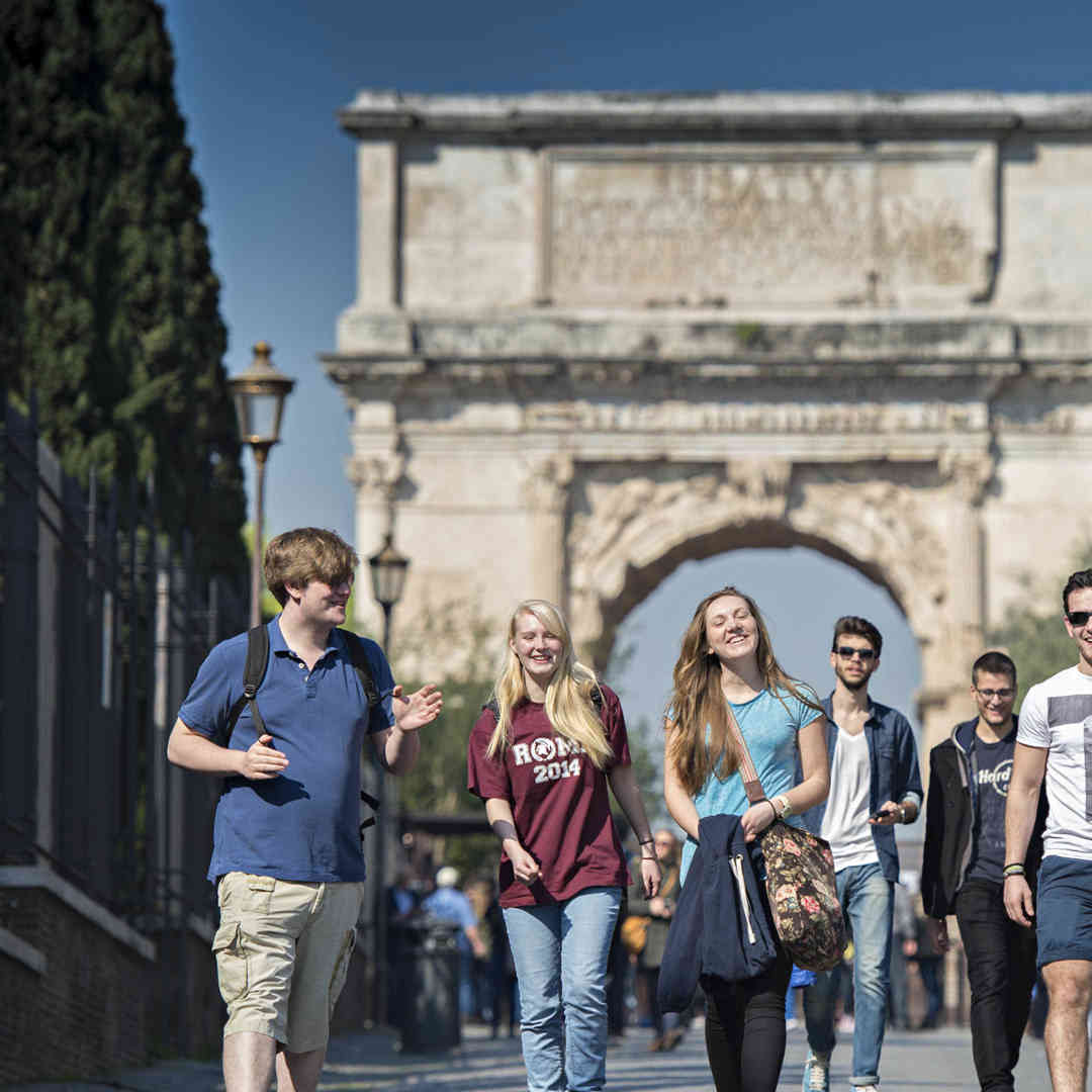 A group of students on a field trip in Rome walk in front of the historic Arco di Tito