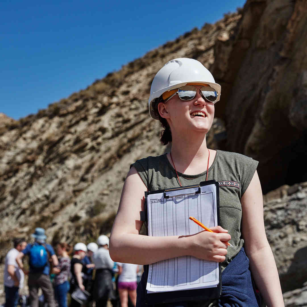 A female Geology student wears a hard hat and holds a clipboard on a Field Trip in Spain