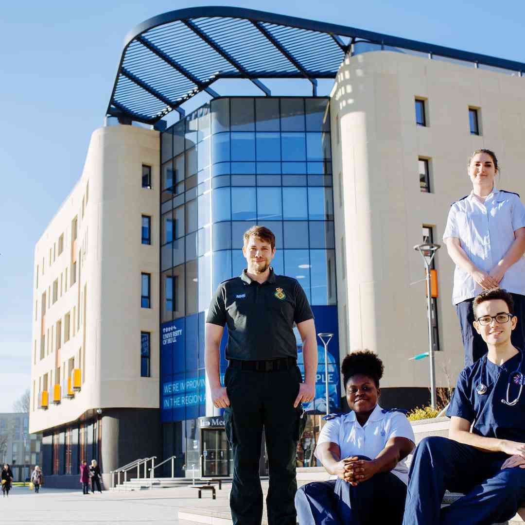 A group of nursing and health students standing in front of the Allam Medical Building wearing different uniforms