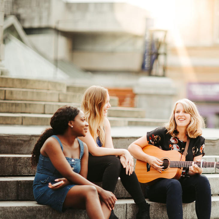 Three music students, one on acoustic guitar, jamming and singing together on Queen Victoria Square steps in Hull.