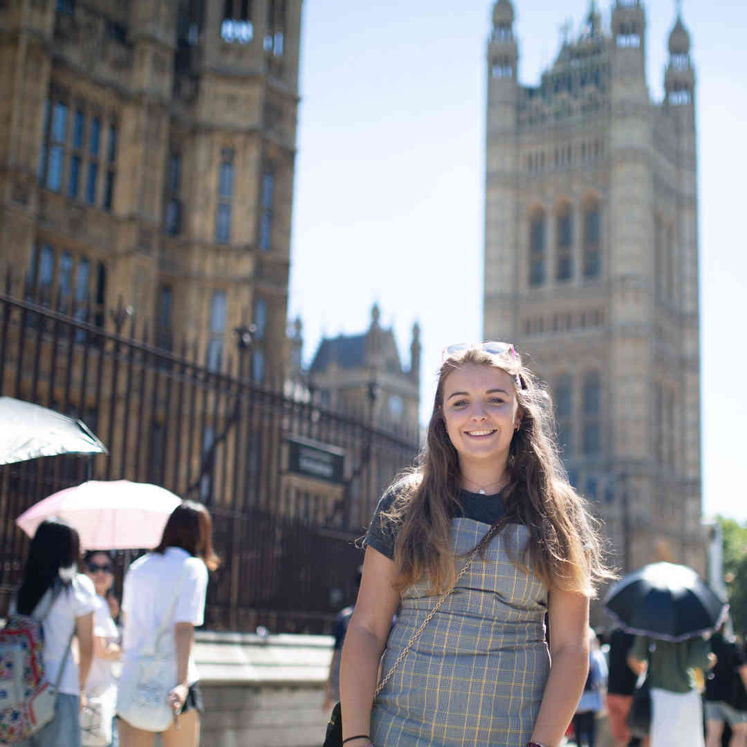 Hull Politics student, Lucy Dunwell, stands smiling outside the Houses of Parliament while a crowd of people walk by.