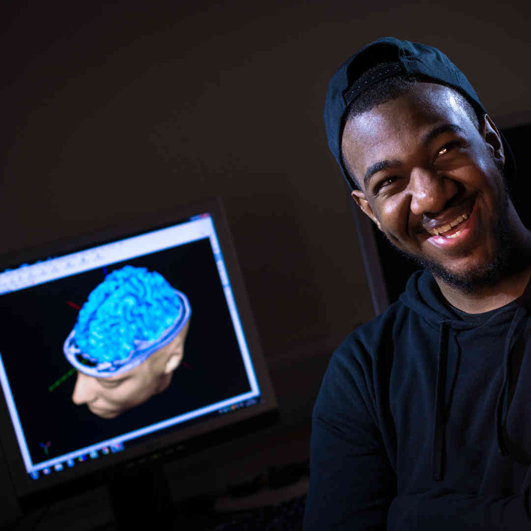 Hull Psychology student, Aaron Hall, smiling in front of a screen showing an animation of a human brain.