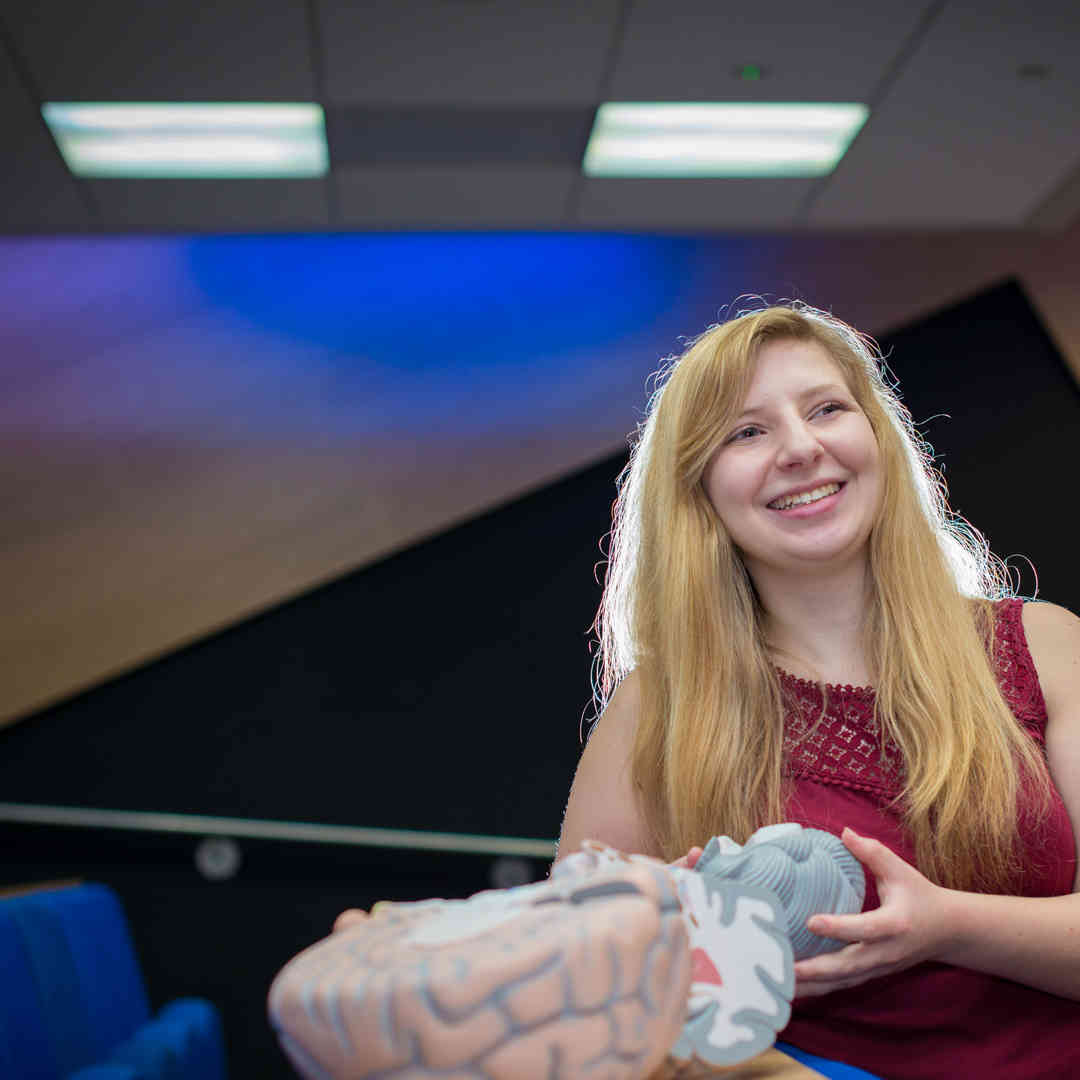 Hull Psychology student, Lisa Stafford, stands smiling holding a model of a brain.