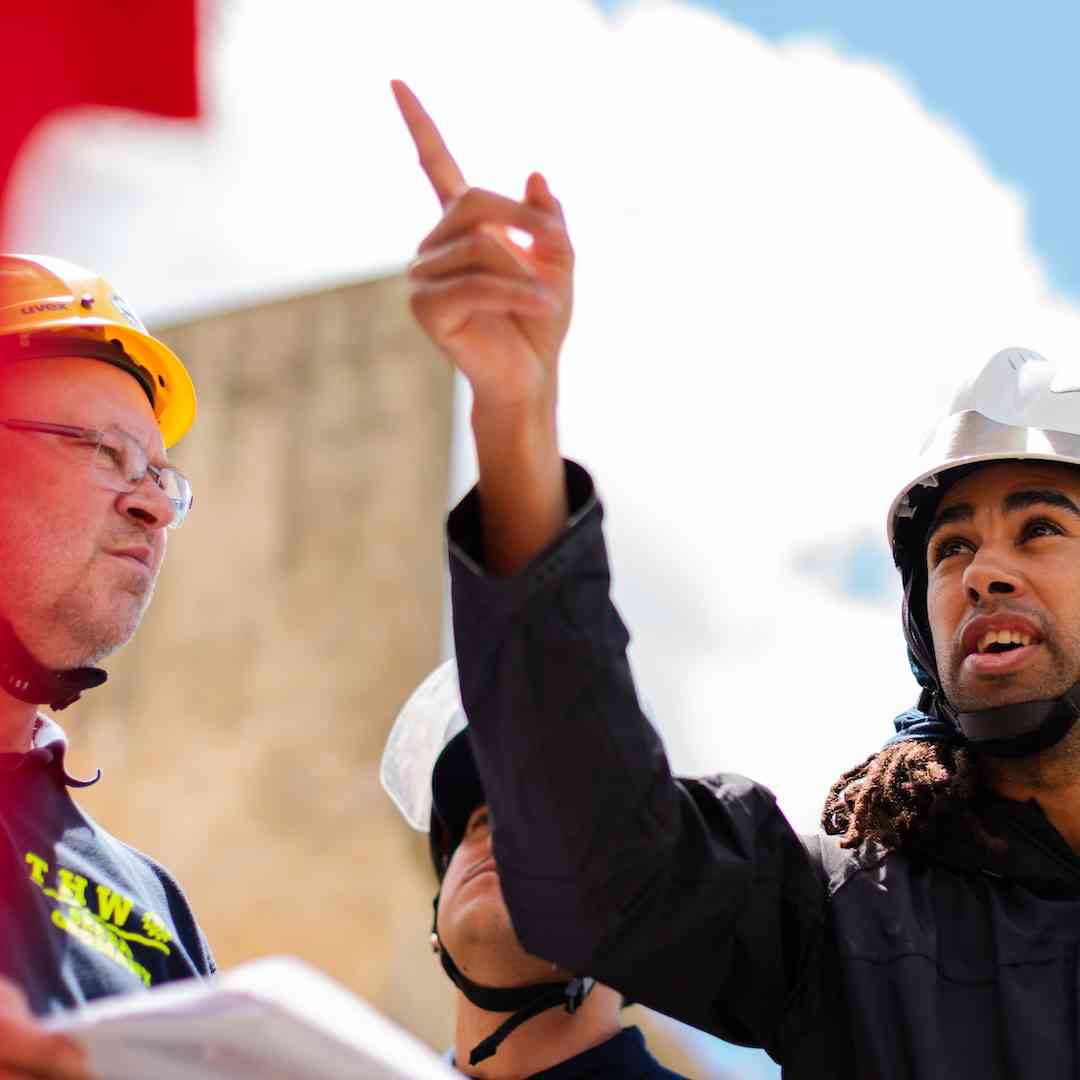 A worker in a hard hat point out something on a building to colleagues