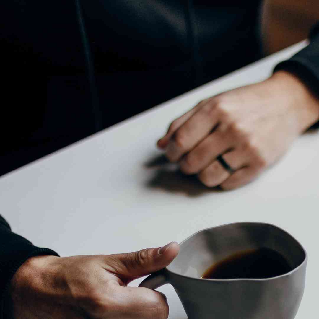 A close up of two people's hands holding mugs of coffee while sat at a table.