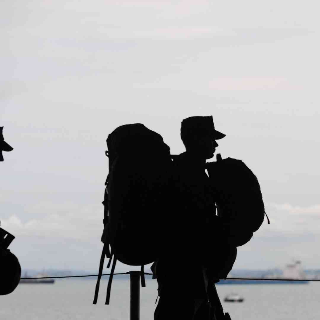 Two soldiers carrying equipment walk along a shoreline