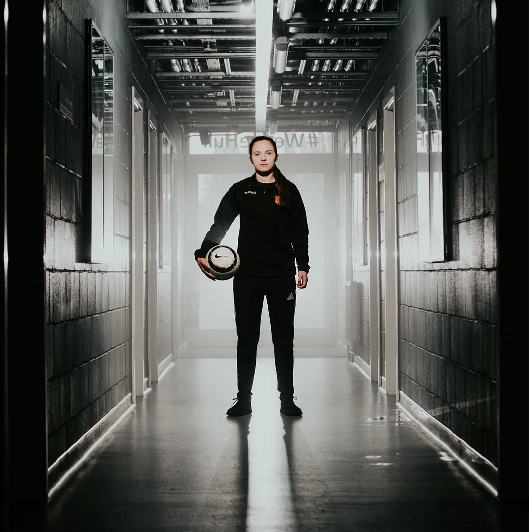 Student standing in hallway with a football under her arm