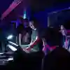 A music lecturer shows functionality of a mixing desk to a group of students crowded round