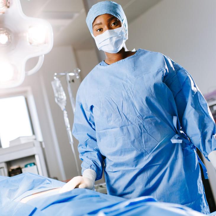 A female student wearing blue scrubs stands in an operating theatre 