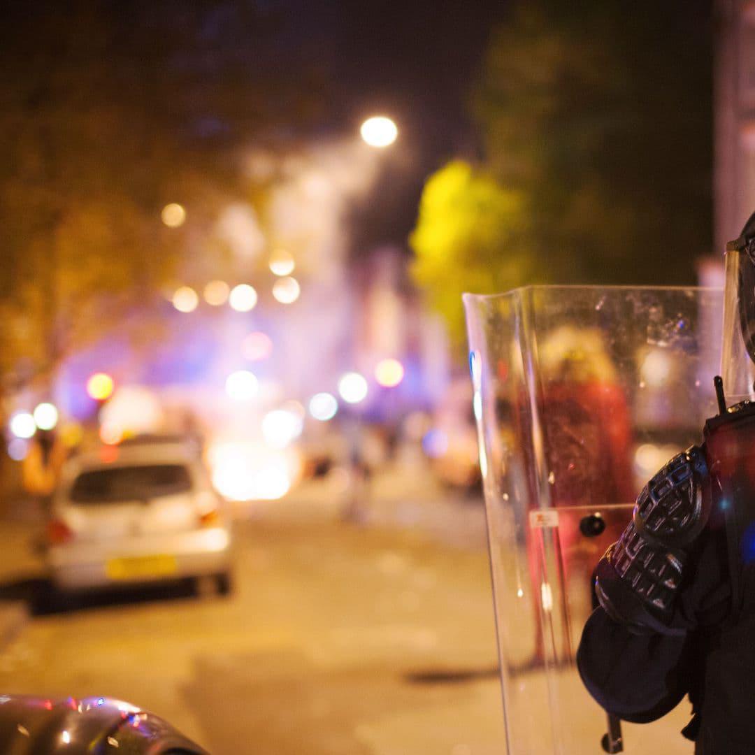 A police officer holding a riot shield standing on the streets of the UK at night