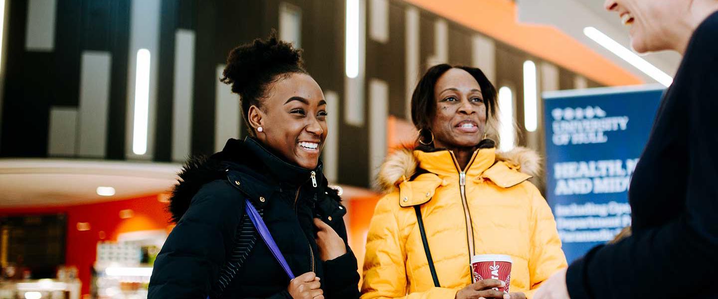 A girl with a purple University of Hull canvas bag over her shoulder speaks to one of our staff with her mum at an Open Day
