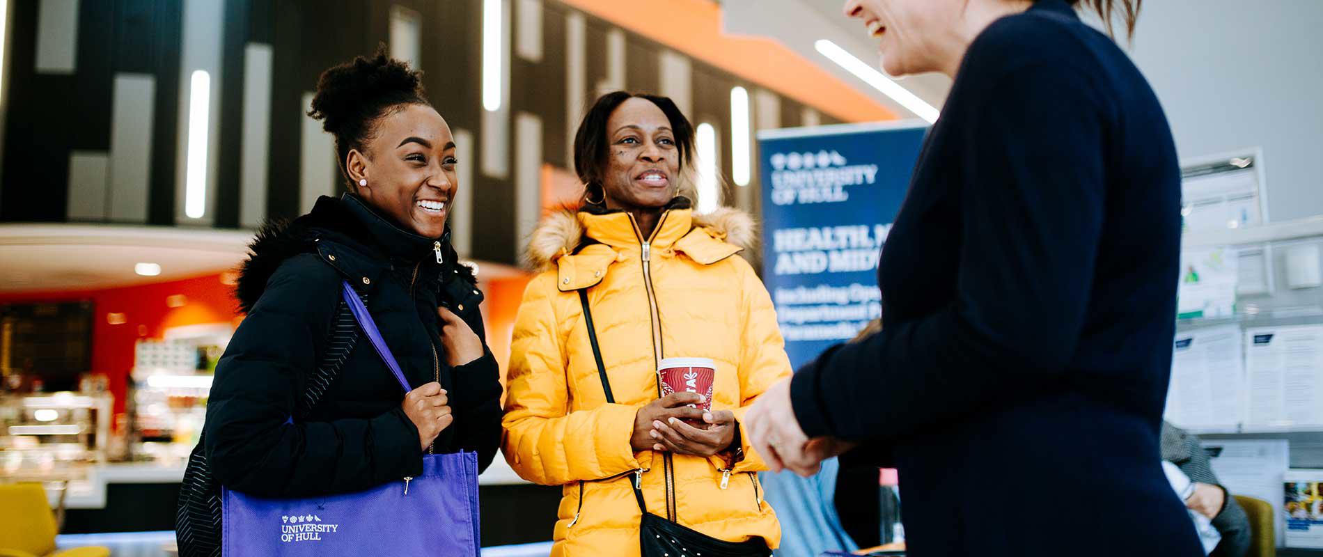 A girl with a purple University of Hull canvas bag over her shoulder speaks to one of our staff with her mum at an Open Day