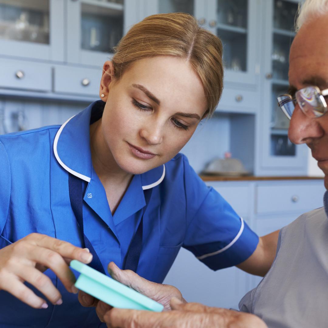 A community nurse wearing a blue uniform shows a patient a piece of equipment
