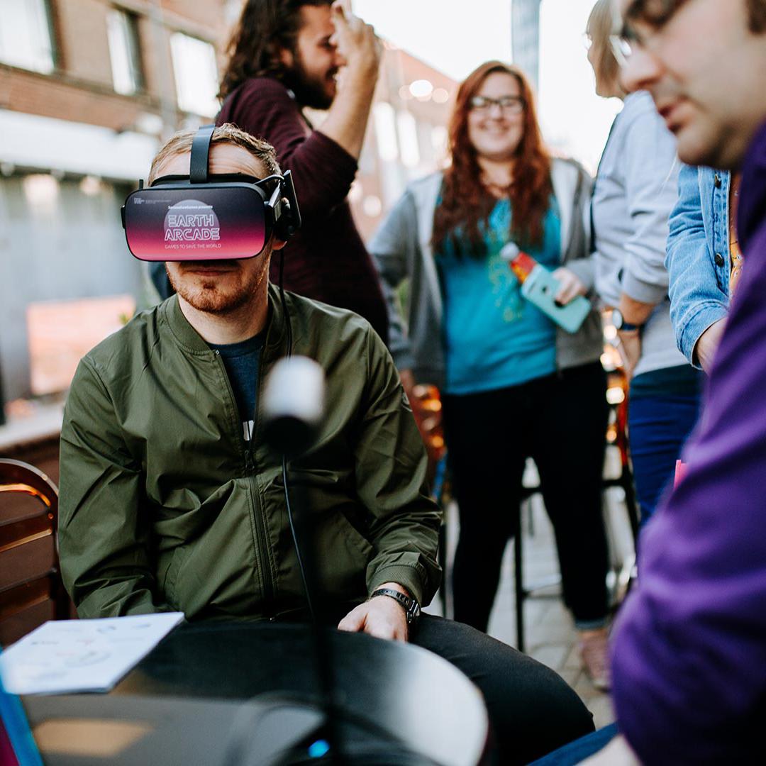 A group of students gather round an outdoor table with one wearing a virtual reality headset
