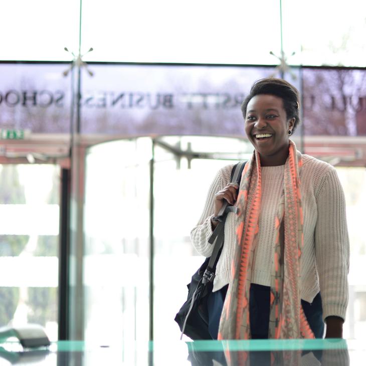 A financial management student smiling while standing in a modern building with a large glass window