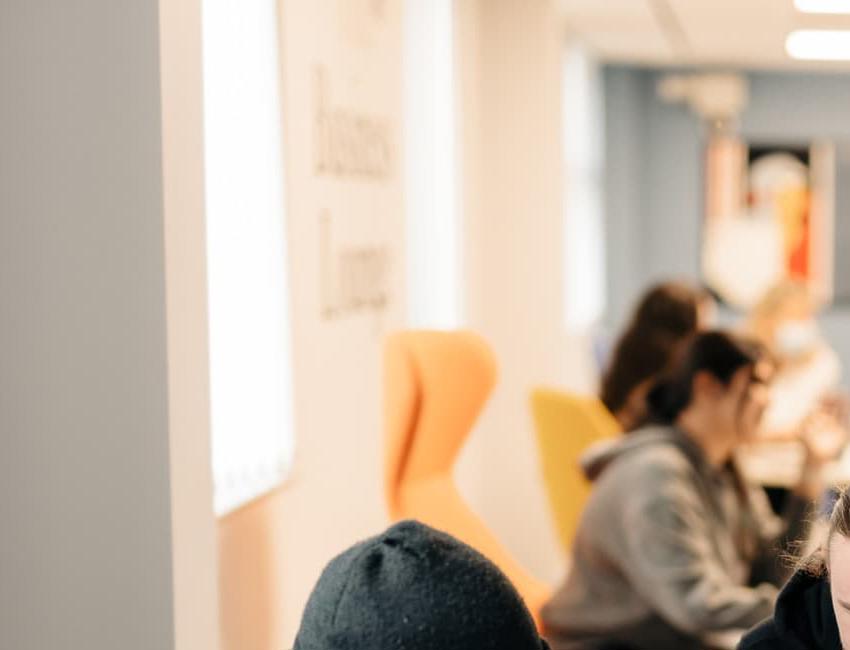 Students gather around an iPad on a table in the new Business Lounge