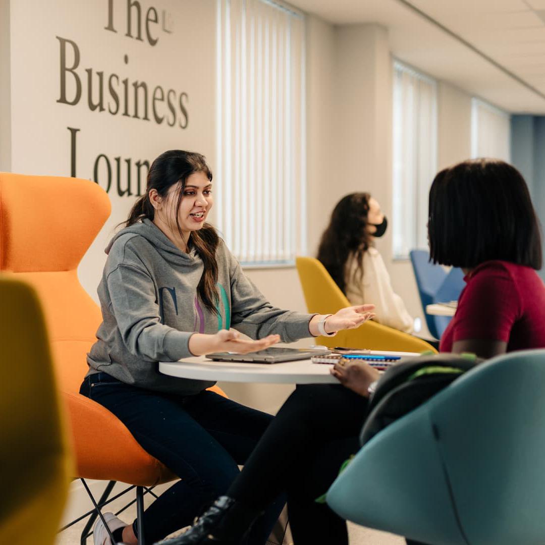 Two female students sat around a table in the Business Lounge