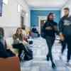 Some students relax in chairs while others walk past them in a modern business school corridor 