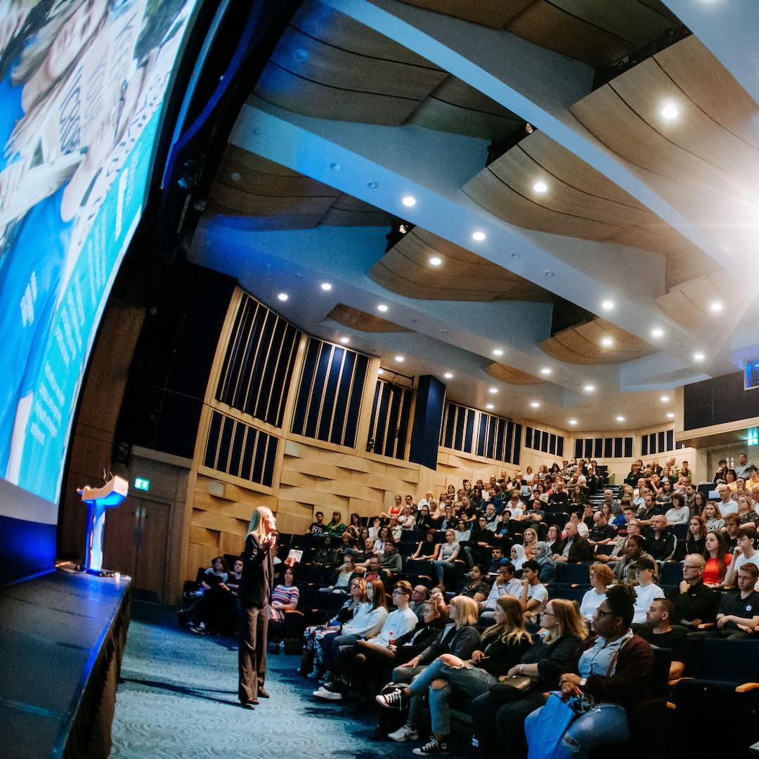 A full crowd in Middleton Hall watches a lecture being delivered