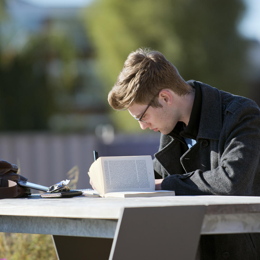 A male student wearing glasses working on a picnic table outside the library