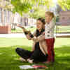 A student sits on green grass next to a young girl