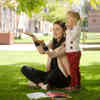 A teacher sitting on grass outside demonstrates to a young child on a sunny day