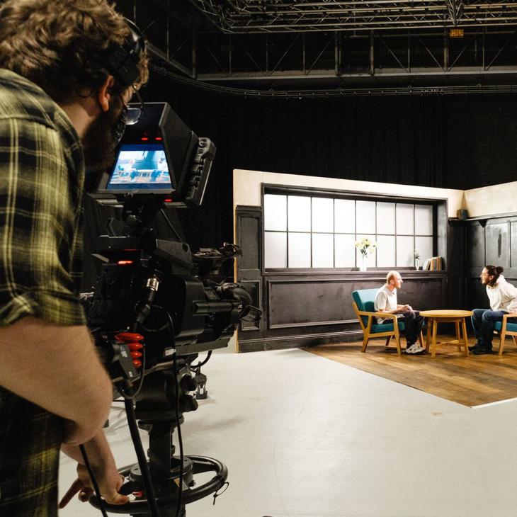 A TV camera films two students on a set