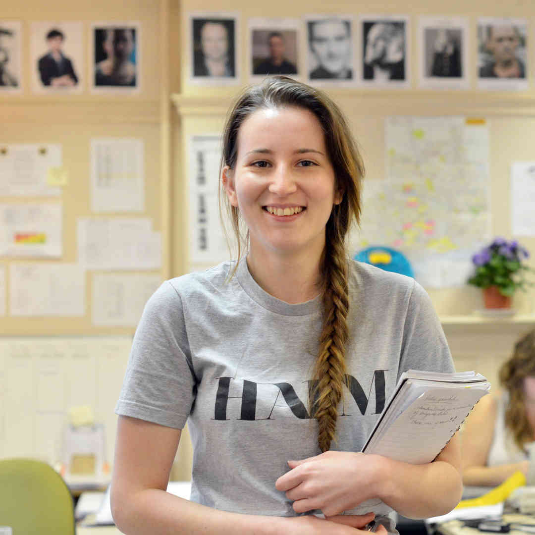 Hull Film Studies student, Lucy Meer, smiling and holding a notepad and pen while students write on laptops behind her.