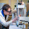 A lecturer wearing a white coat and protective goggles working on a piece of equipment in a lab 