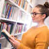 Hull Geography student, Rhianna Phillips, reading a book while browsing the bookshelves of the Brynmor Jones Library.