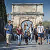 A group of students on a field trip in Rome walk in front of the historic Arco di Tito