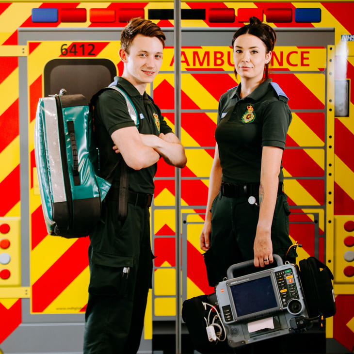 two male and female student paramedics stood in front of mock ambulance