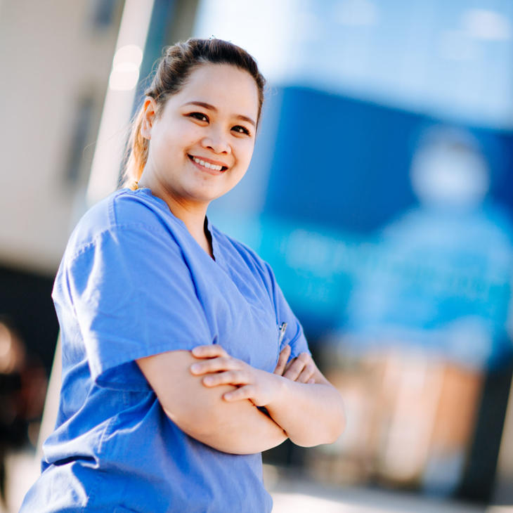 A medical student in blue scrubs outside the Allam Medical Building