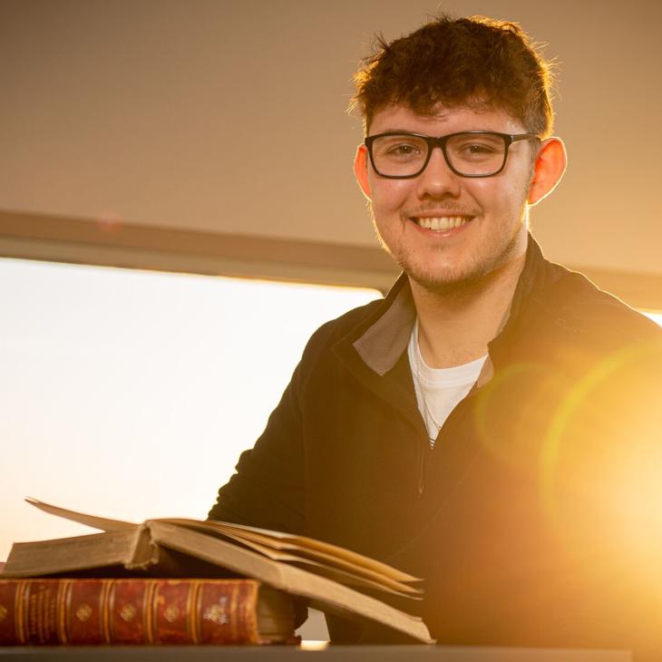 A History student sitting in the library with a book on the desk in front of him