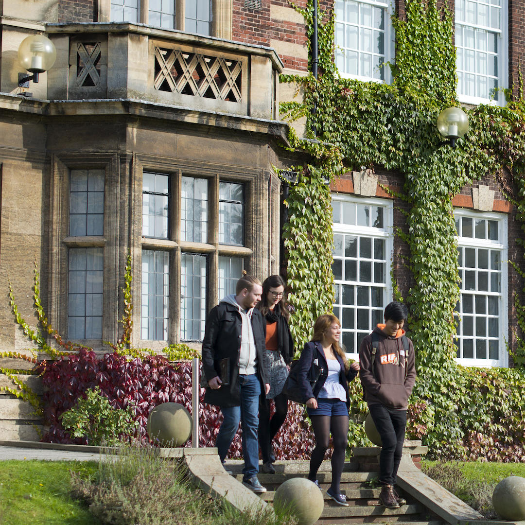 Business students walking down the steps in front of an ivy-covered building in the Business School 