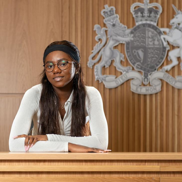 A law student poses in front of the UK royal coat of arms in a mock courtroom