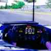 A view from the cockpit of a race car simulator showing the steering wheel and a race track on a large screen