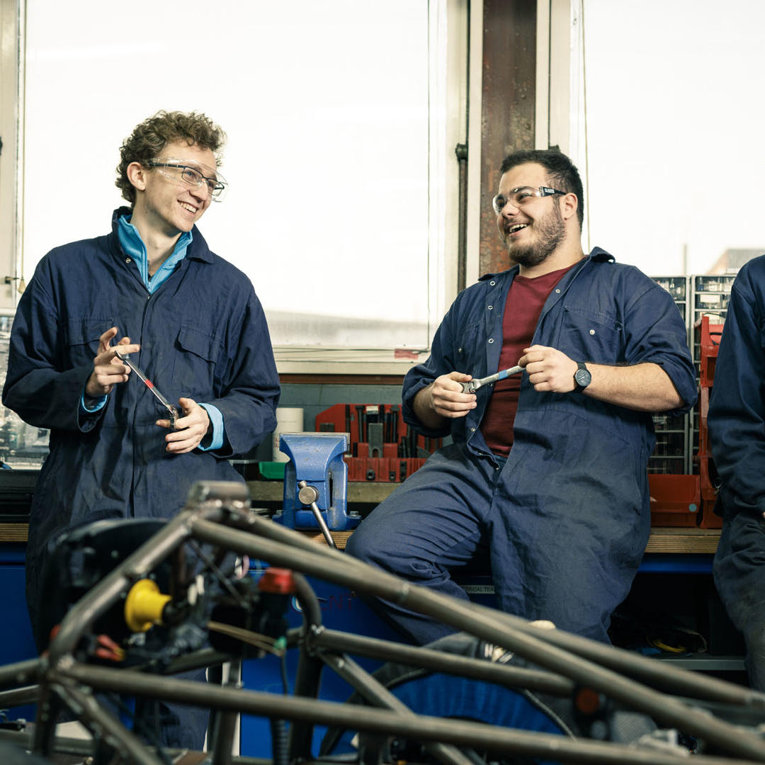 Three students in mechanic's overalls standing in a workshop 