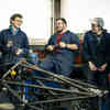 Three students in mechanic's overalls standing in a workshop 