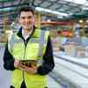 An Mechanical Engineering Intern in a high vis vest standing in a manufacturing warehouse 