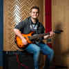 Hull Music student, Alexander Duffell, sits smiling on an amp while holiding a guitar in a recording studio.