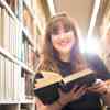 Hull Philosophy student, Clara Wisenfeld-Paine, smiling with an open book while browsing the bookshelves of the library.