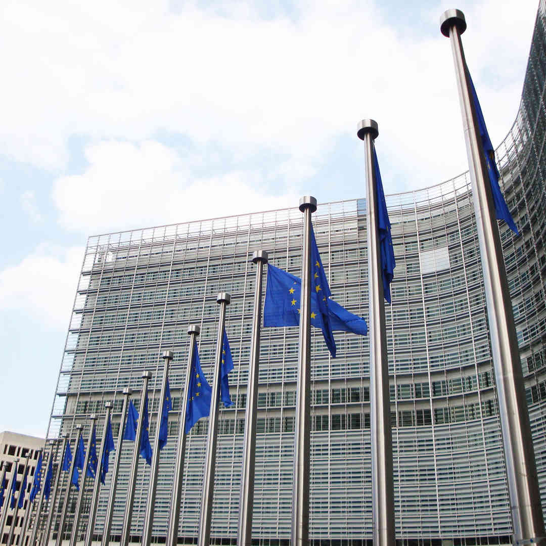 The European Union headquarters in Brussels. A modern steel and glass building surrounded by EU flagpoles.